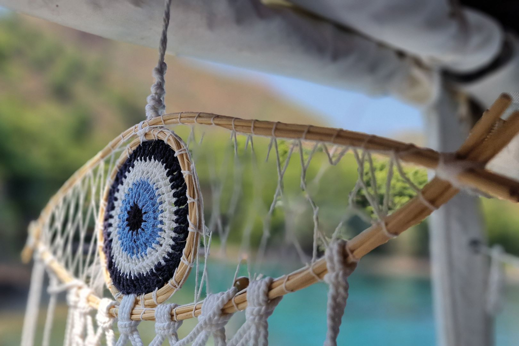 Ein kunstvoller Traumfänger hängt an einem Schiffsbalken mit Blick auf üppiges Grün und blaues Wasser.