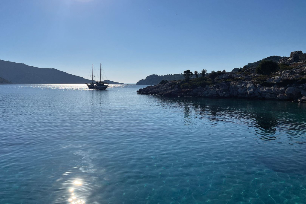 Türkises Meer mit einer Yacht und felsiger Küstenlinie unter blauem Himmel.