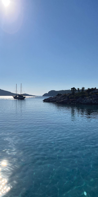 Panorama von tiefblauem Meer mit klarem Himmel, einer felsigen Insel und einem Segelboot.
