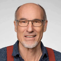 Porträt eines lächelnden, baldigen Mannes mit Brille, der direkt in die Kamera blickt.