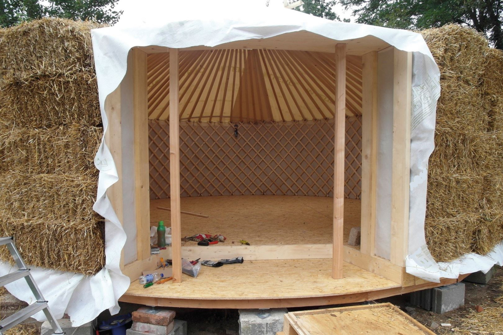 Ein temporär errichtetes Holzspielhaus, das von hohen Strohballen flankiert wird.
